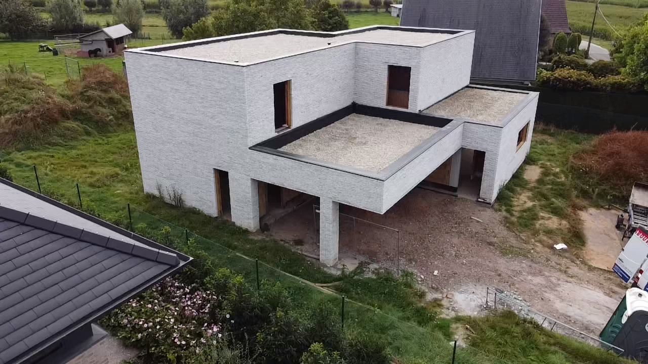 Luchtfoto van een kubistische nieuwbouwwoning met strakke lijnen en een plat dak in wit kiezel op EPDM, in een landelijke omgeving